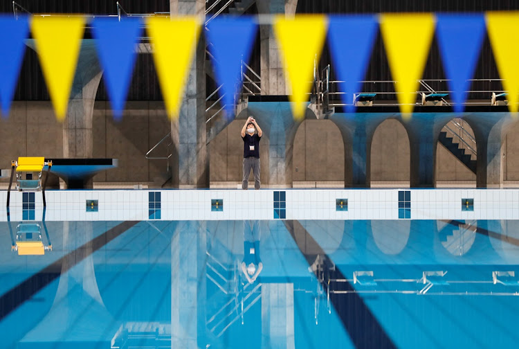 A man wearing a protective face mask is reflected on the surface of the swimming pool at Tokyo Aquatics Centre, which hosted the artistic swimming, diving, and swimming events at the Tokyo Olympic and Paralympic games.