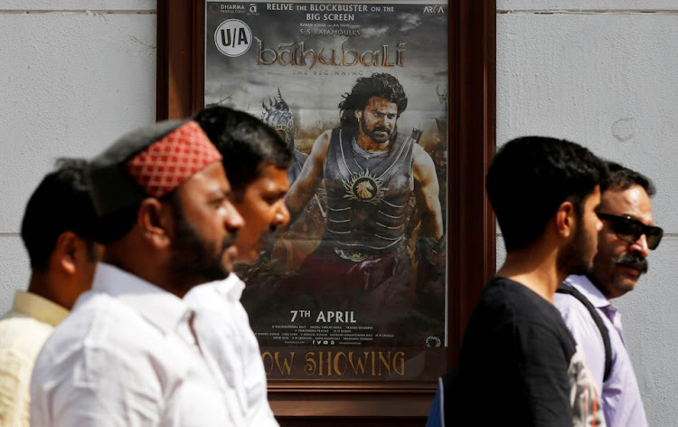 People walk past a poster of an Indian movie "Baahubali: The Beginning" outside a movie theater in New Delhi, India, April 12, 2017.