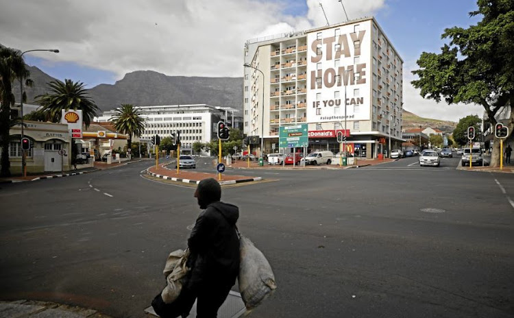 A man walks past a building in Cape Town covered with a poster aimed at limiting the spread of Covid-19.