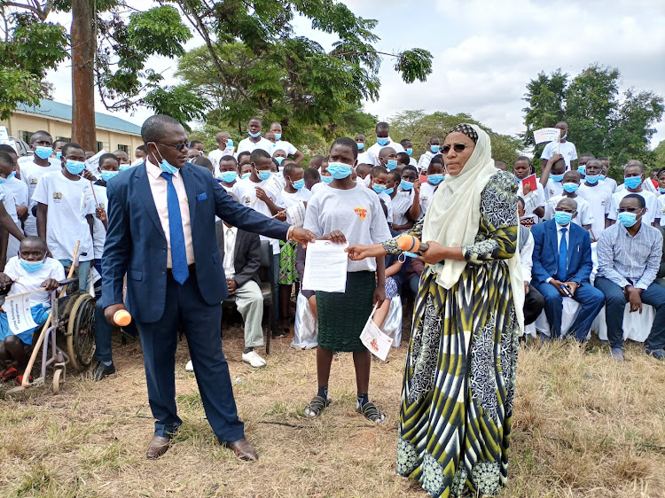 Equity Bank Kitui manager Francis Mbindyo and Kitui Central director of education Marry Channo gives an award letter to a Wings to Fly scholarship beneficiary at Kitui High School grounds on Tuesday.