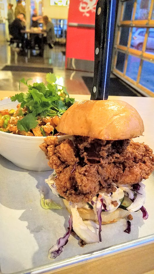 Basilisk Fried Chicken Sandwich with fried chicken thigh and house pickled cucumbers, shredded cabbage and special sauce that needs a knife stabbed through the middle to keep it together