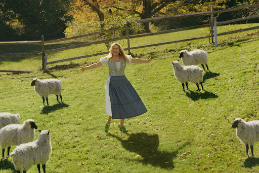 Jennifer Coolidge in a field surrounded by sheep.