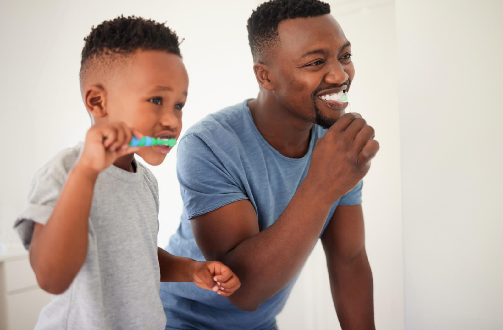 A father teaching his young boy to brush his teeth in the bathroom.