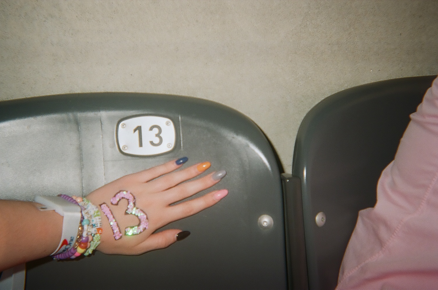 A girl’s hand with a 13 painted on it held up against a seat with the number 13.