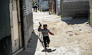 A child carrying a toy gun runs through Marikana informal settlement in Cape Town, where 11 people were murdered in a shooting spree in 2018.