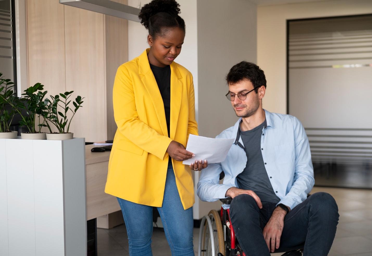 A person looking at a paper while a person sits in a wheelchair

Description automatically generated