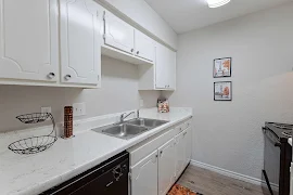 Galley style kitchen with white cabinets and countertops, stainless steel sink, and black appliances 