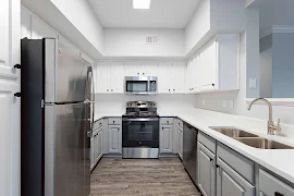 Kitchen with white upper & grey lower cabinets, white quartz countertops, stainless steel appliances, wood floors