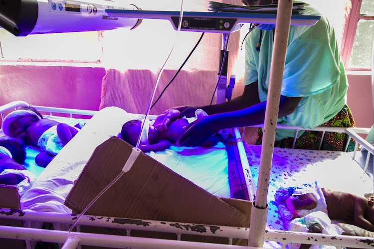 A mother checks on her newborn baby girl with eyes covered, undergoing light therapy due to jaundice through a process called called phototherapy