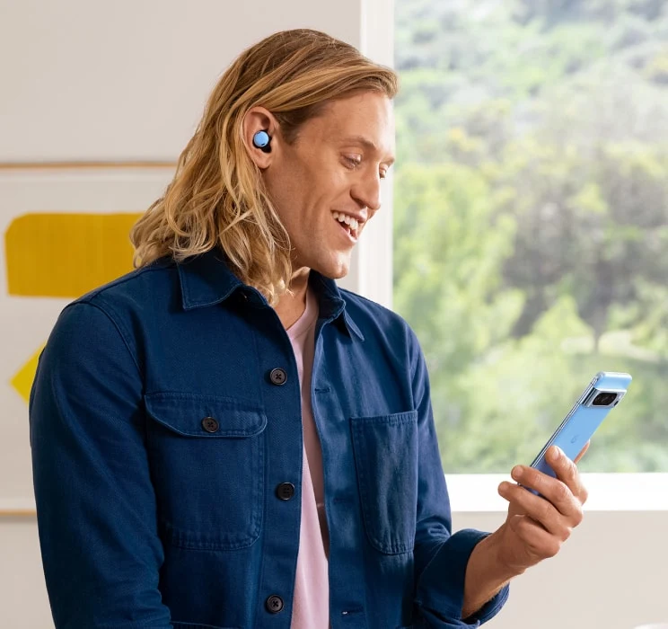 A person wearing Pixel Buds in Bay colour holds their Pixel 8 Pro in Bay colour.