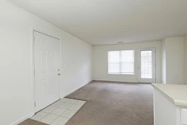 Carpeted living area featuring front door with tiled entrance, large window, and large window in patio/balcony door