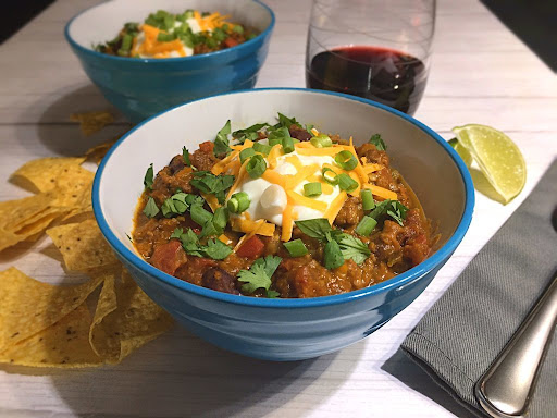 A delicious bowl of Pumpkin Chili topped with sour cream, shredded cheese, cilantro and green onions.