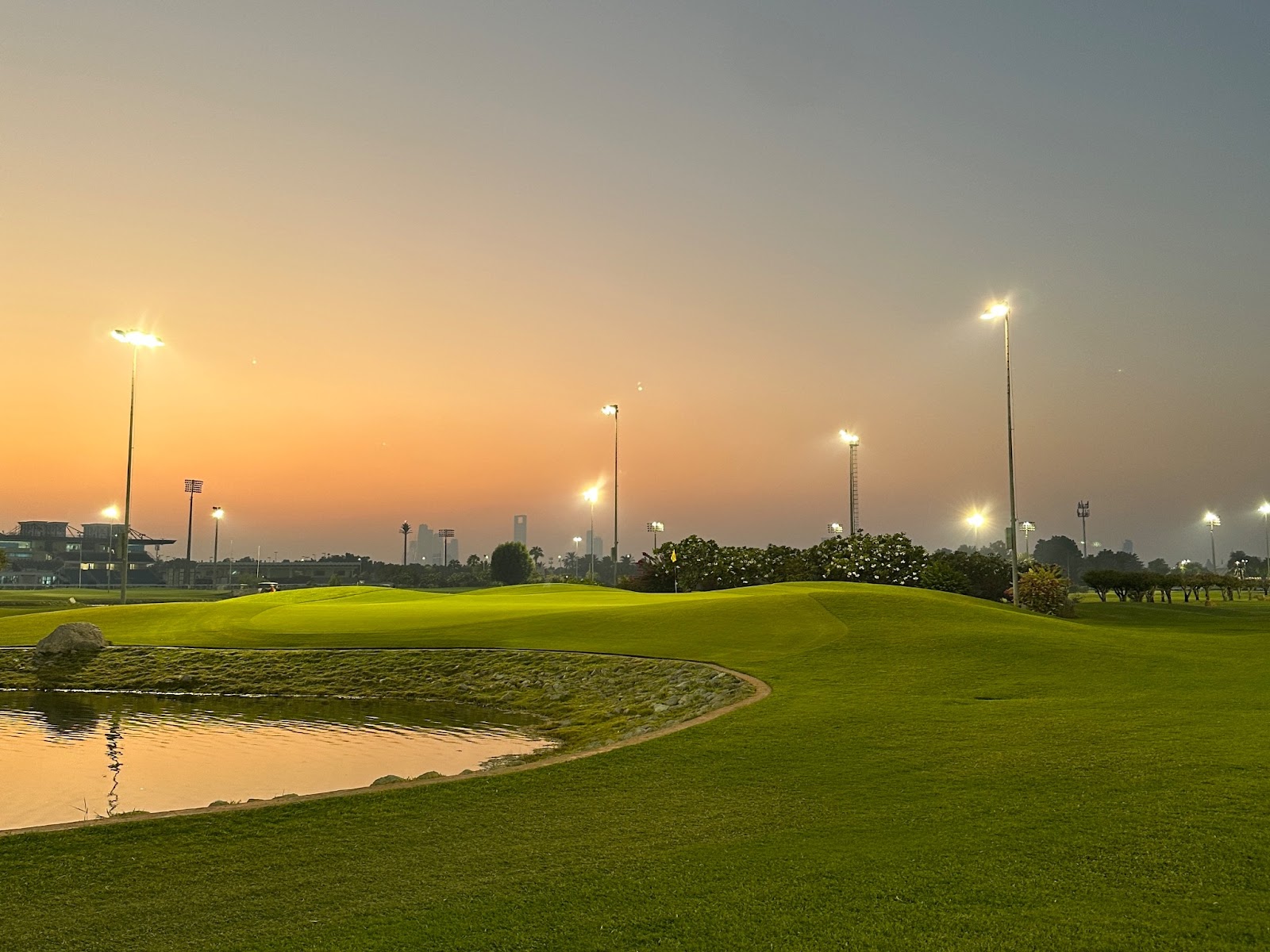 Abu Dhabi City Golf Club: Green fairways, city skyscrapers, and a serene lake at sunset, next to the Abu Dhabi Equestrian Club.