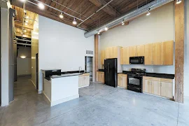 Kitchen with cement flooring, black countertops, light wooden cabinets, black appliances, high wooden ceilings, and a pantry