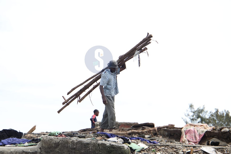 A man carries logs of woods after demolitions at Mukuru kwa Njenga on May 6, 2024.