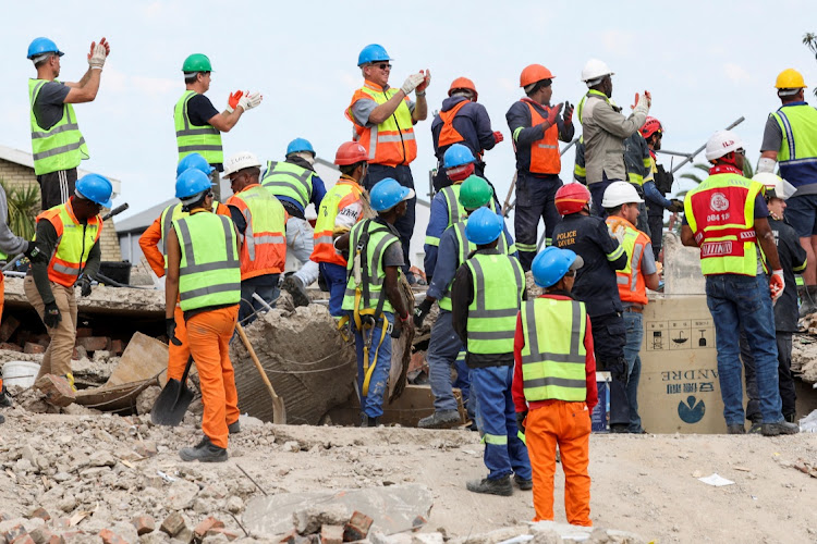 Rescuers celebrate after saving a construction worker trapped under a building that collapsed in George.