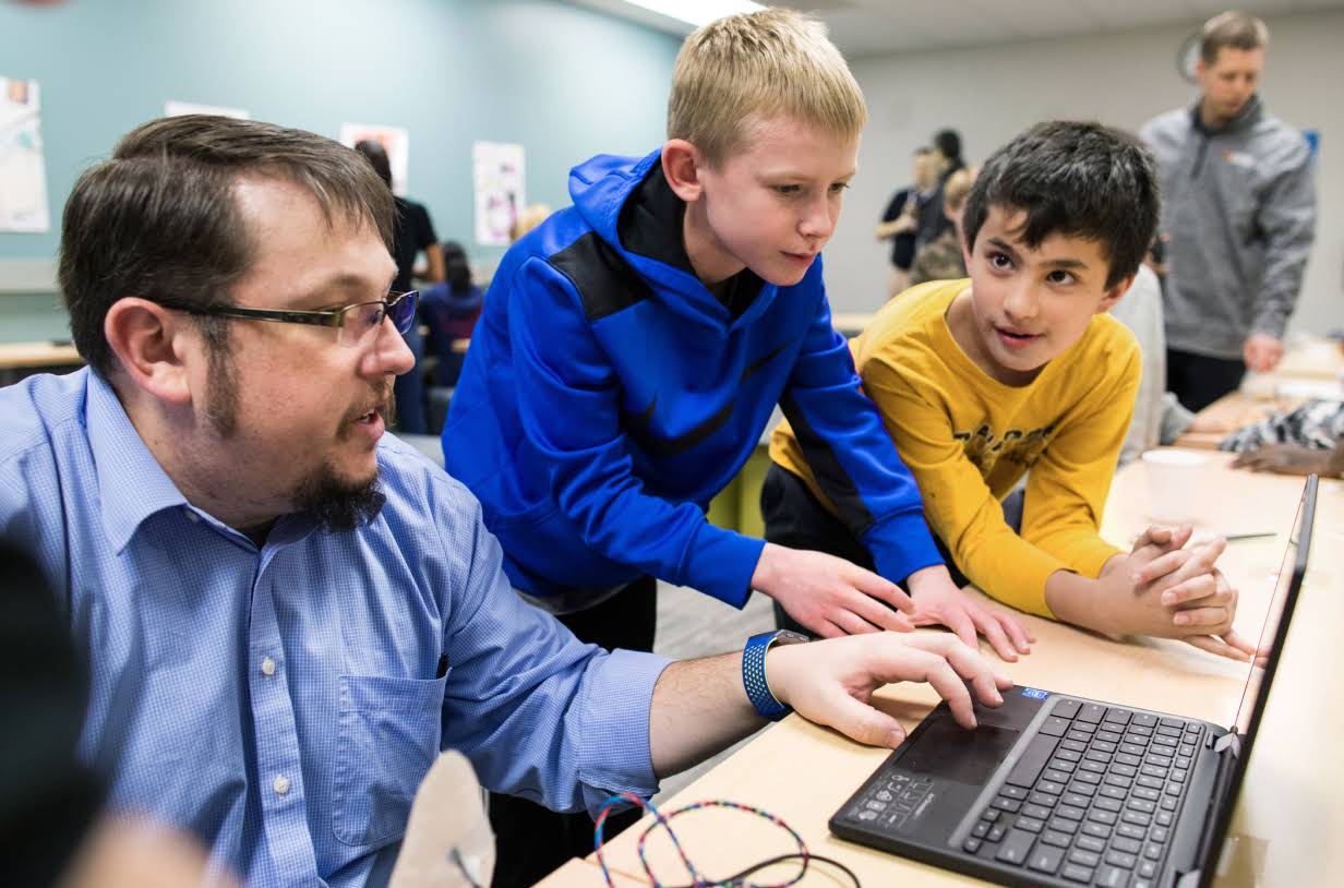 Un profesor ejecuta una demostración en una laptop para dos alumnos.