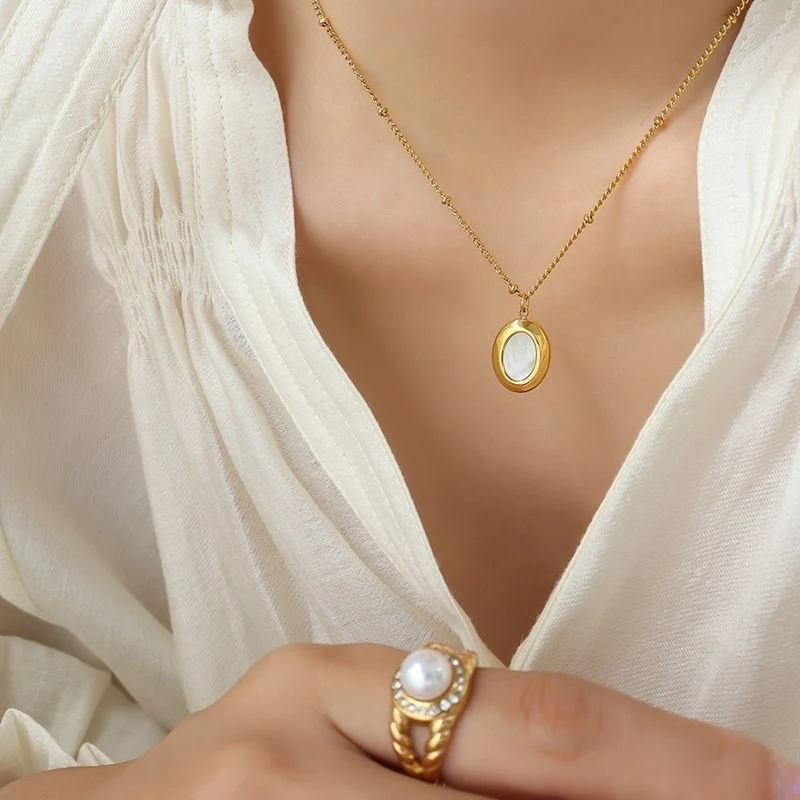 Collier pendentif ovale en coquillage naturel, chaîne à billes et acier titane plaqué or K pour clavicule. Élégance naturelle.