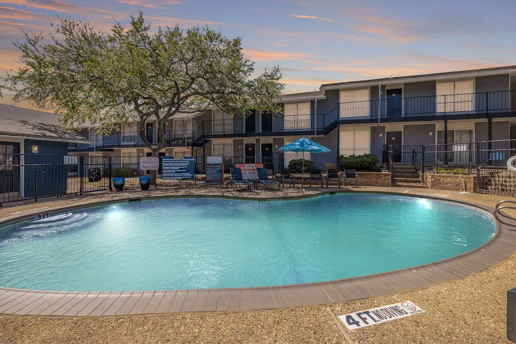 Mustang Villlas community fenced-in swimming pool at dusk with lounge furniture, blue apartment buildings in background