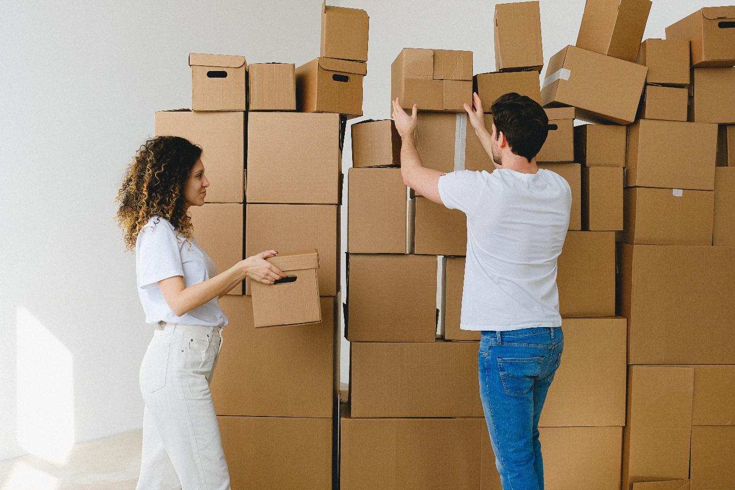 Two people standing next to a pile of boxes  Description automatically generated with low confidence