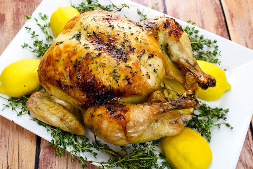 Maple-Butter Roasted Chicken on a serving tray with thyme and lemons.