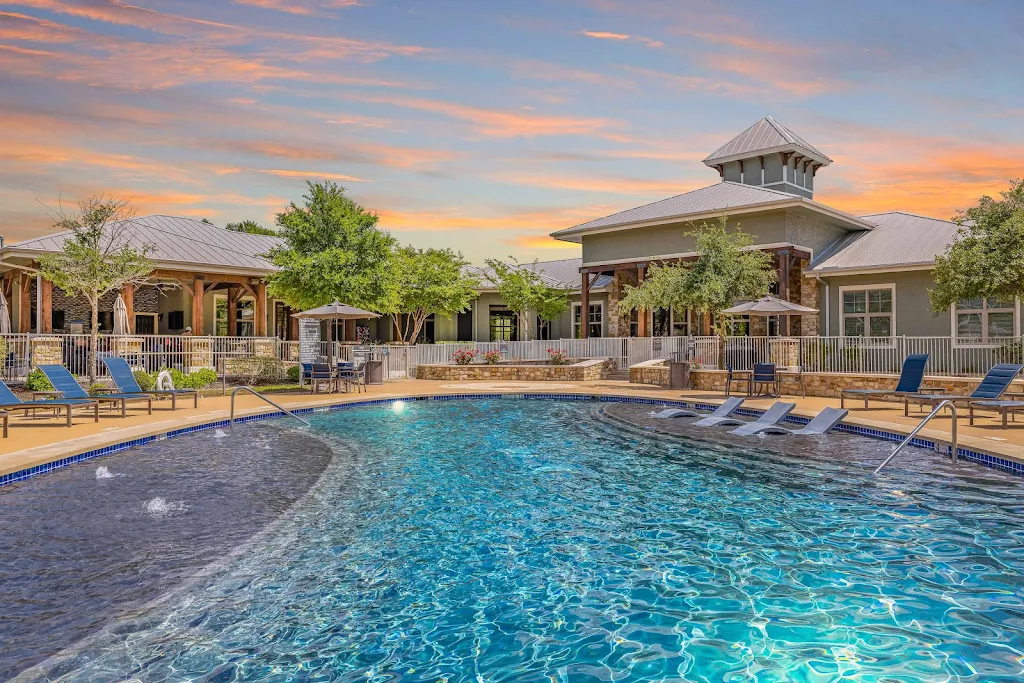 Resort style swimming pool with lounge chairs on the pool deck and apartment buildings in view at dusk 