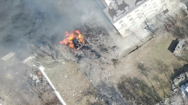 An aeriel view showsa military vehicle on fire next to a building, as Russia's invasion of Ukraine continues, in Maripuol, Ukraine as uploaded on March 13, 2022, in this handout drone video obtained by Reuters on March 13, 2022. Picture: HANDOUT via REUTERS