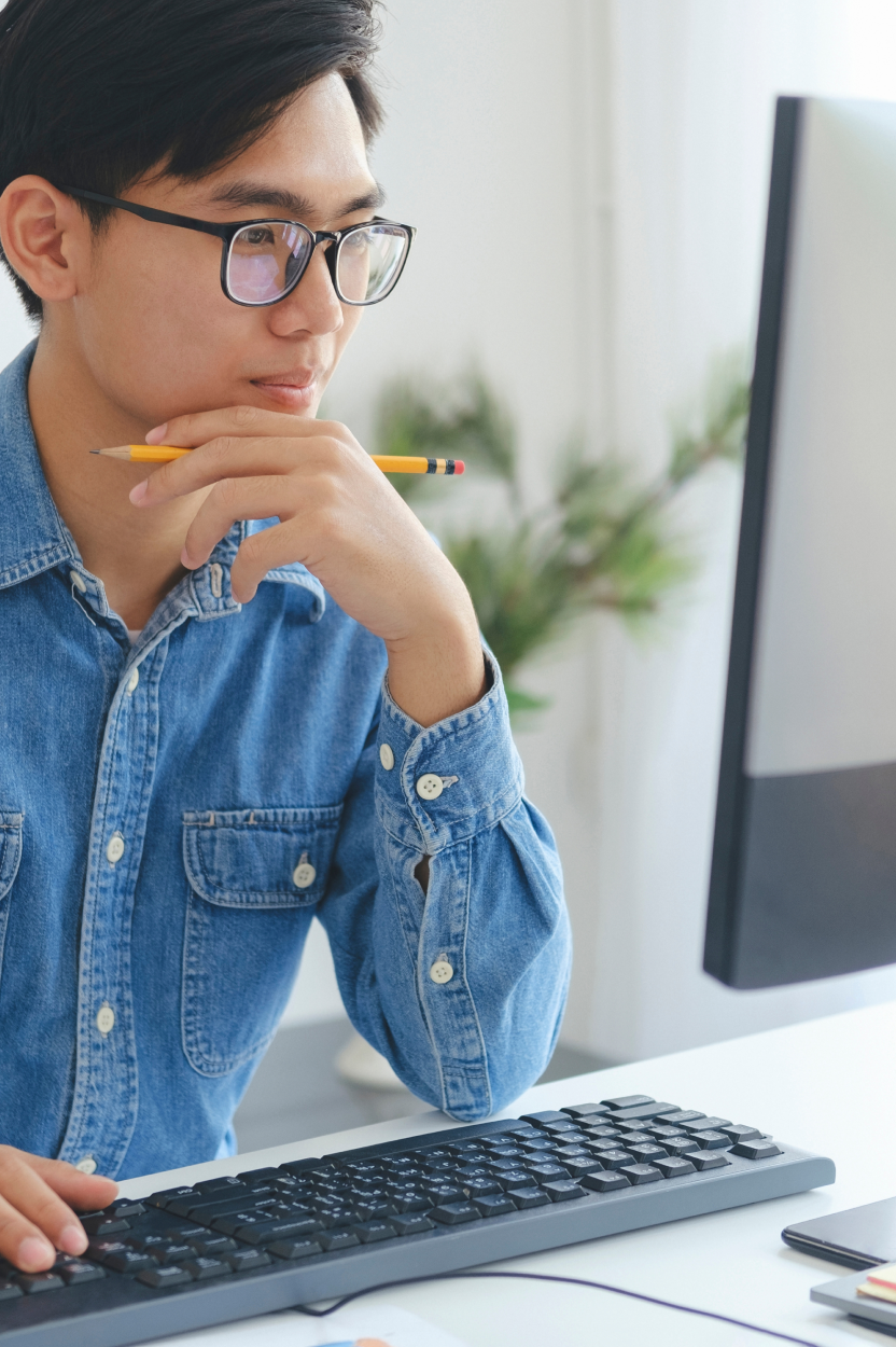 A man holding a pencil and looking at a computer monitor.