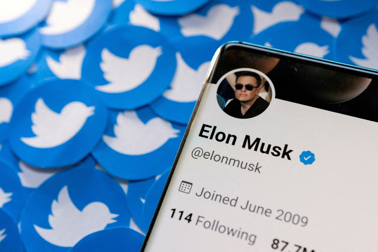 Elon Musk's Twitter profile is seen on a smartphone placed on printed Twitter logos.