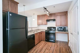 Kitchen with wood flooring, marble-inspired counters, dark wood cabinets, black appliances and track lighting