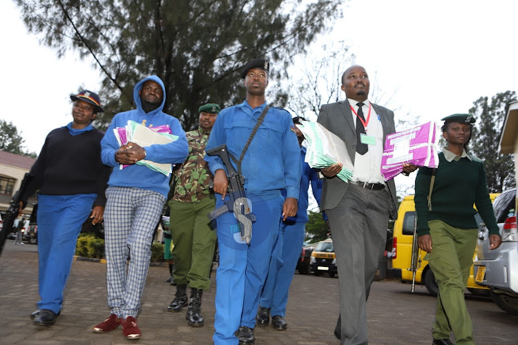 Anajali Primary School headteacher Dickson Onyango and Kilimani Junior Academy headteacher Samuel Muriithi are escorted after picking KCPE exam papers at Langata DCC, Nairobi on November 28, 2022.