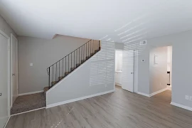 Living room with carpeted staircase up to second level, light wood plank flooring, light gray walls and white trim and doors