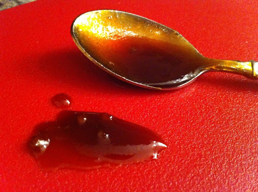 Sauce in the spoon with more besides it on a red cutting board.