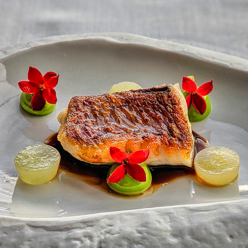 juicy delicious gourmet meal decorated with three red flowers served on a white plate. Delicacy served at Restaurant Azurmendi in Bilbao Spain.