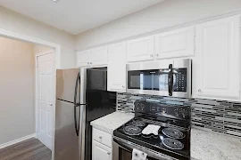 Kitchen with stainless steel appliances, white cabinets, light gray speckled countertops, and gray toned backsplash