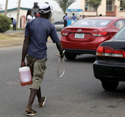 A petrol hawker walks with petrol in a container towards a car, in Abuja, Nigeria.