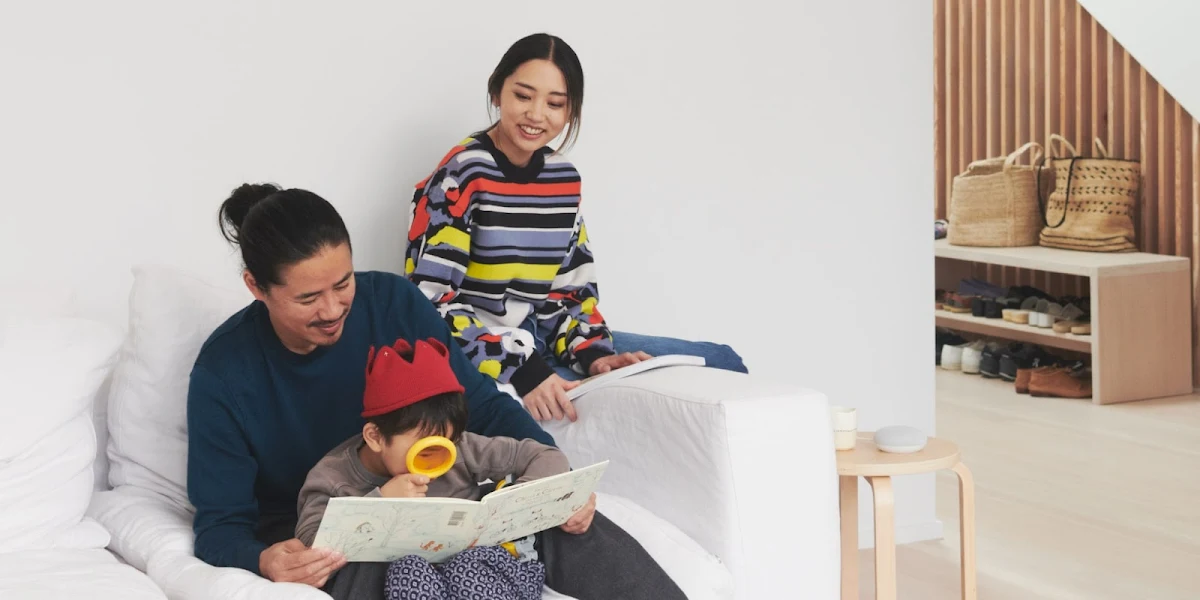 Two parents sit together with their child, who is reading a book with a magnifying glass