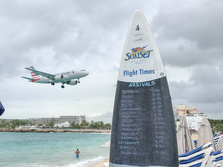 A surfboard on Maho Beach lists the scheduled landing times of flights, including this American airline.