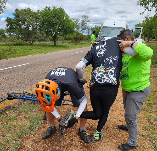 Global cyclist Steve Keet, of Kidds Beach, performs on-road repair on Jimbo Armstrong's "laughing shoe" - a strap is repurposed - while team doctor and support crew member, paediatrician surgeon, Dr Mia Elsen, lends a shoulder.