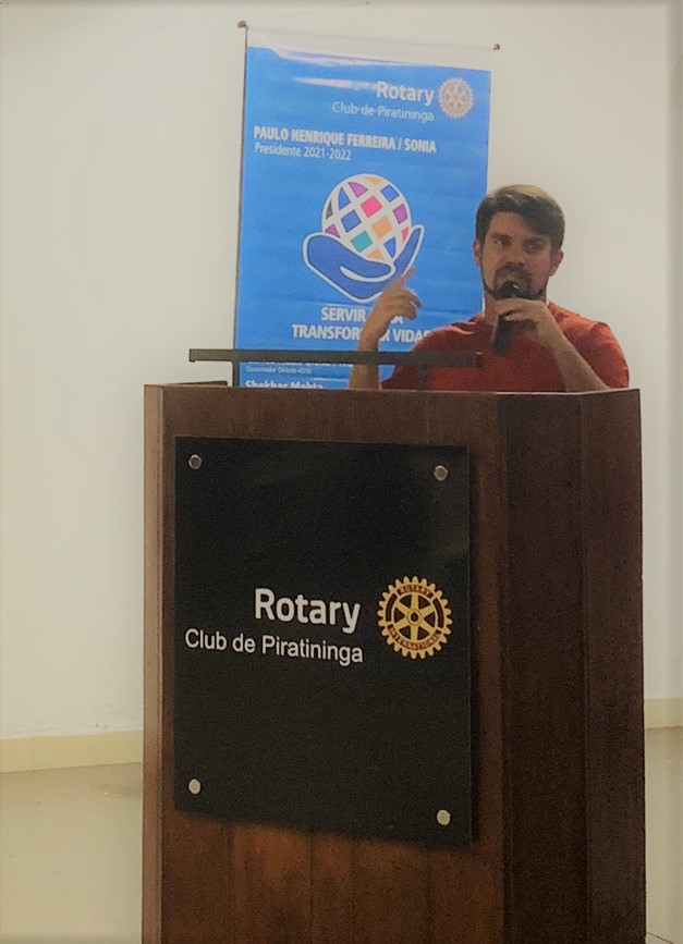 um homem branco num palanque de discurso com a placa “Rotary Club de Piratininga”