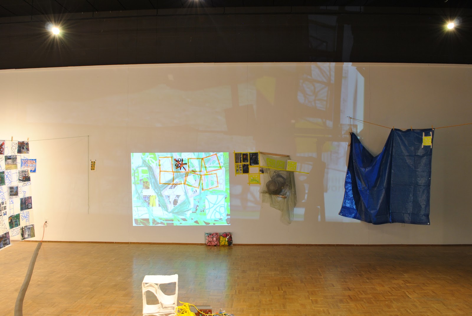 Image: Kelly Clare, enter / the net / here, 2022, installation view, Edna Carlsten Gallery. Projected images are flanked by hanging quilts and tarps in the gallery space. Image courtesy of the artist.