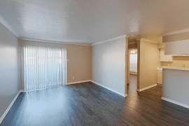 Open concept living room, next to kitchen, with wood plank floors, sliding glass patio door with blinds, and light color scheme