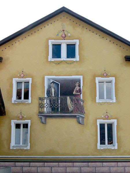 This photo shows a unique balcony facade illusion. A man and a woman appear to be standing outside on the balcony when in fact they are just drawn onto the wall of the building. There are also a number of vases that appear to be sitting on the window frames but they too are just drawn illusions.