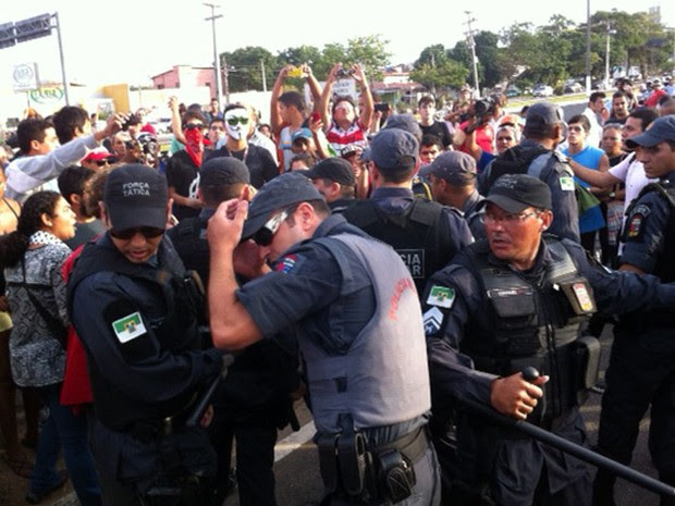 Policiais militares se protegem de pedras atiradas por manifestantes durante protesto na inauguração da Arena das Dunas, em Natal (Foto: Felipe Gibson/G1)