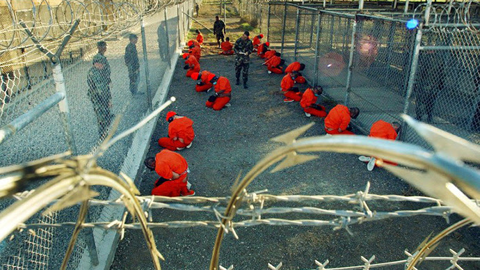 Detidos em macacões laranja sentar-se em uma área de exploração sob o Surveillence de policiais militares dos EUA em Camp X-Ray em Base Naval de Guantánamo, em Cuba.  (AFP Photo / Shane T. Mccoy)