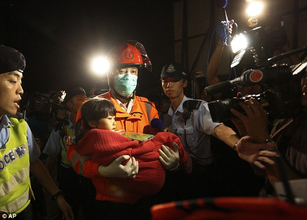 Ordeal: Wrapped in a red blanket to keep warm, a girl is brought to safety by a rescuer wearing a facemask