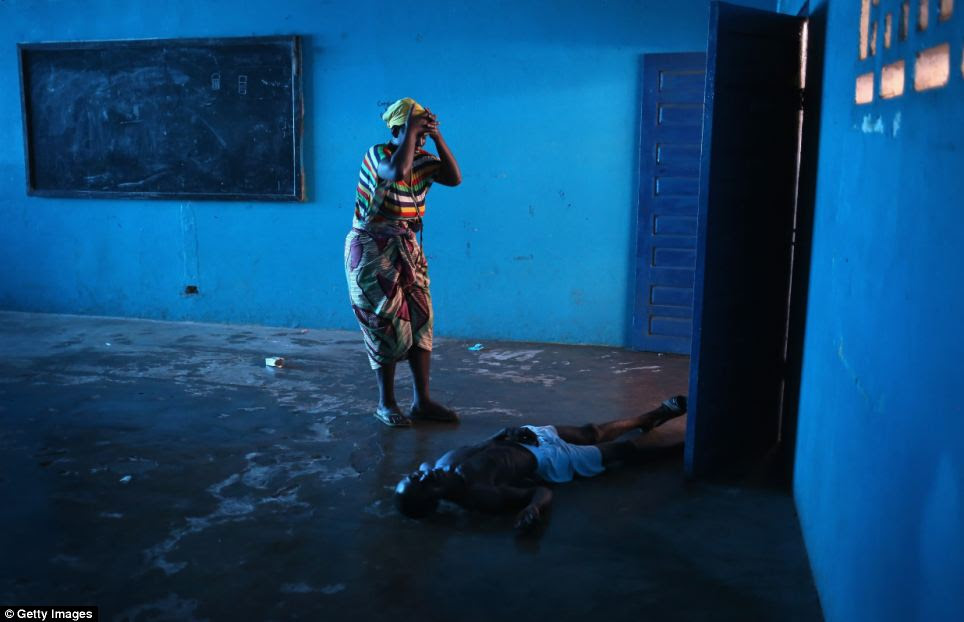 A woman stands over her husband with her head in her hands, after he staggered and fell, knocking him unconscious in an Ebola ward in Liberia