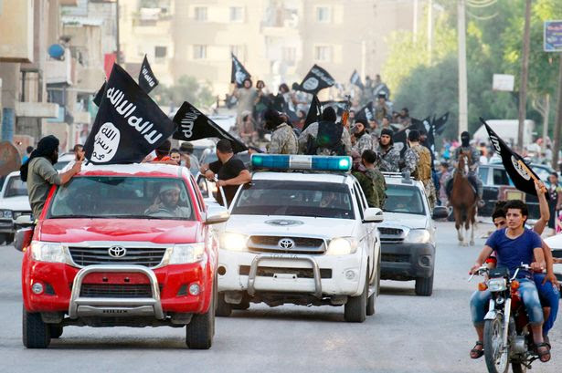 Militant Islamist fighters waving flags, travel in vehicles as they take part in a military parade along the streets of Syria's northern Raqqa province 