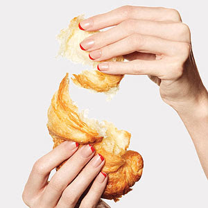 Hands with red French manicure holding croissant
