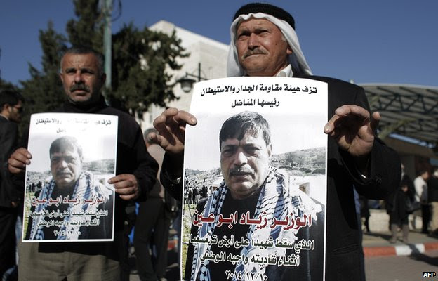 Palestinian men carry posters bearing the portrait of Cabinet member Ziad Abu Ein, after the announcement of his death outside the main hospital in the West Bank city of Ramallah on December 10, 2014